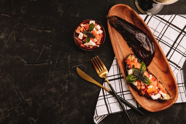 Melanzane al forno con insalata di pomodori, formaggio feta e basilico su un piatto di legno