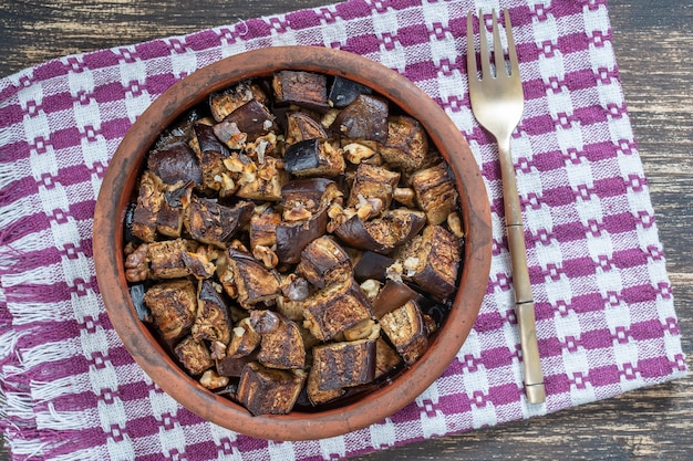 Melanzane al forno con noci, olio d'oliva e spezie su un piatto sul tavolo di legno. Cibo vegetariano. Primo piano, vista dall'alto