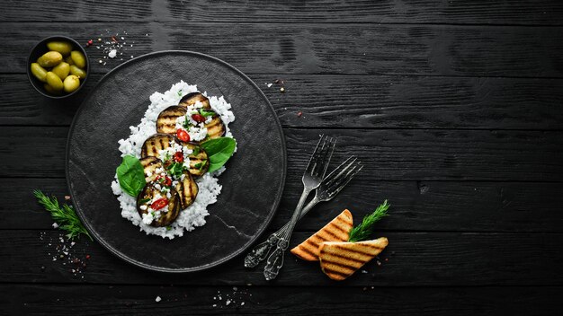 Melanzane alla griglia con riso e formaggio su un piatto nero Vista dall'alto Stile rustico