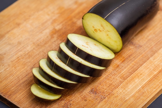 Melanzane fresche a fette sul tagliere di legno isolato sul nero. Ingredienti da cucina