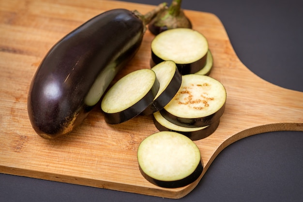 Melanzane fresche a fette sul tagliere di legno isolato sul nero.