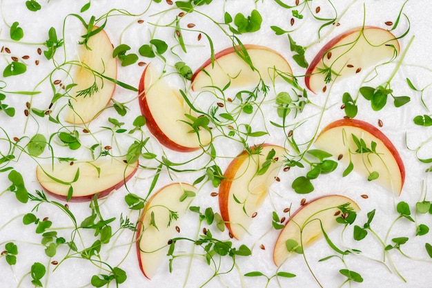 Mele a fette con giovani germogli microgreen su sfondo bianco, alimentazione sana.