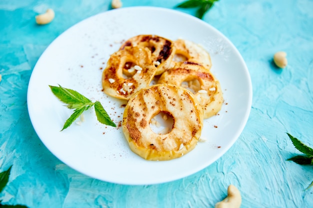 Mele arrostite con cinamon sul piatto bianco su fondo blu.