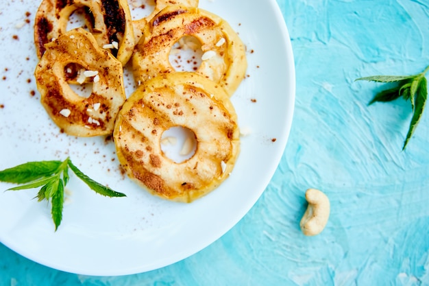 Mele arrostite con cinamon sul piatto bianco su fondo blu.