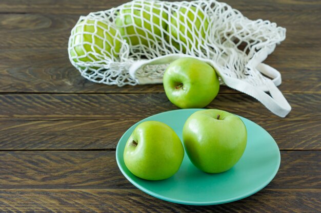 Mele biologiche Granny Smith su un piatto con borsa in tessuto a rete su un tavolo di legno.