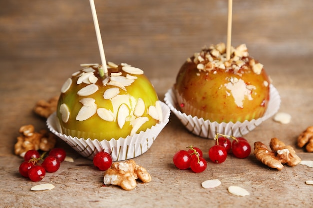 Mele caramellate dolci su bastoncini con frutti di bosco, su tavola di legno wooden