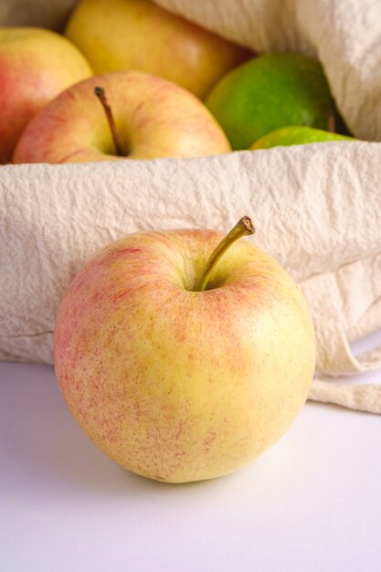 Mele dolci fresche nella borsa di drogheria riutilizzabile del tessuto su superficie bianca, macro di vista di angolo