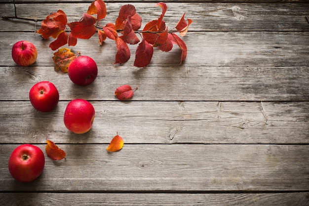 Mele e foglie rosse su vecchio fondo di legno