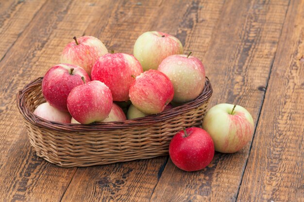 Mele mature rosse in canestro di vimini sui bordi di legno vecchi.