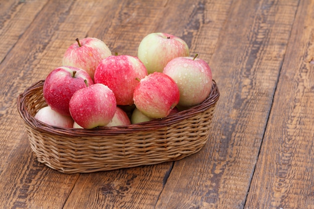 Mele mature rosse nel canestro di vimini sui bordi di legno vecchi.