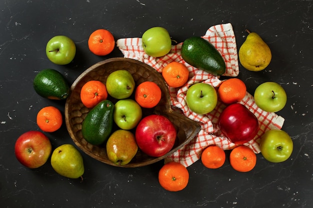 Mele, pere, arance e avocado in ciotola in legno intagliato su marmo nero come tavola, vista dall'alto