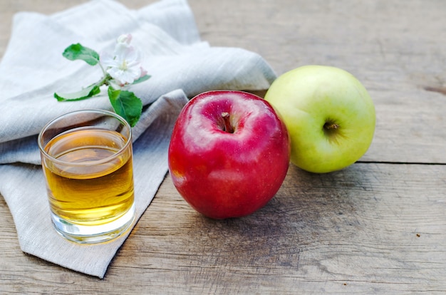 Mele rosse e gustose con un bicchiere di sidro (succo di mela) sul tavolo di legno