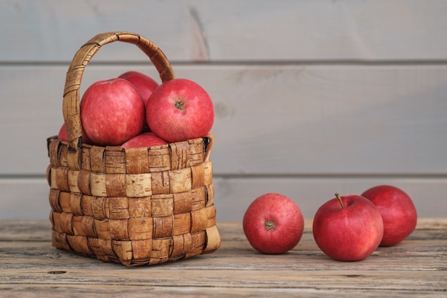 Mele rosse mature dal giardino in un cesto di vimini vintage su una vecchia tavola