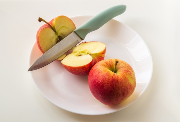 Mele rosse mature nel piatto con un coltello. Taglia una mela prima di mangiare per seguire la dieta