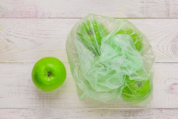 Mele verdi fresche nel sacchetto di plastica sulla tavola di legno. concetto ambientale di uso non ecologico della plastica