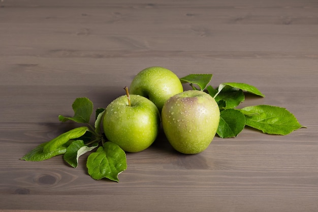 Mele verdi mature fresche e foglie di melo su uno sfondo di legno