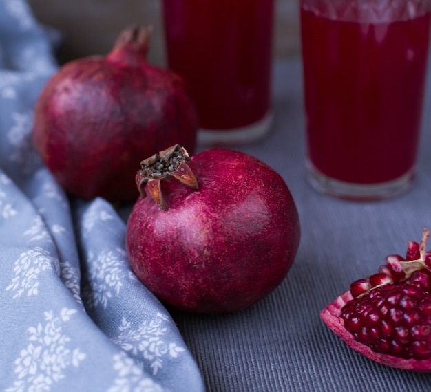 Melograni e succo di melograno in un bicchiere su una tovaglia grigia