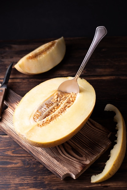 Melone mezzo maturo con semi e cucchiaio sul tagliere su fondo di legno scuro.