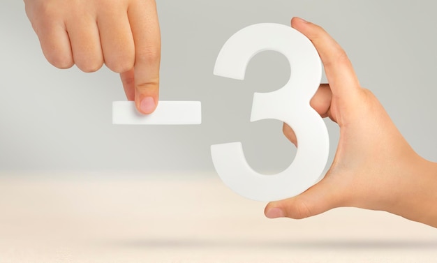 Meno tre il numero tre e il simbolo meno in un primo piano della mano su uno sfondo grigio chiaro il c