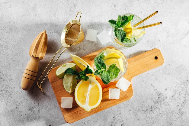 Menta, lime, ghiaccio al limone e utensili da bar su tagliere di legno su sfondo di marmo bianco vista dall'alto