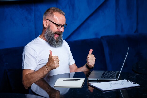 Mentore maschio adulto, direttore, uomo d'affari con gli occhiali e un vestito che studia documenti mentre è seduto al tavolo. Concetto di giornata lavorativa