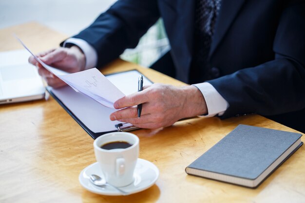 Mentore maschio adulto, direttore, uomo d'affari con gli occhiali e un vestito che studia documenti mentre è seduto al tavolo. Concetto di giornata lavorativa