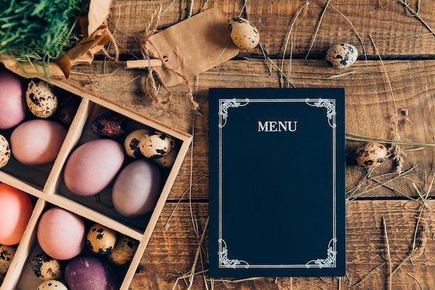 Menù di Pasqua. Vista dall'alto delle uova di Pasqua in scatola di legno e scheda menu sdraiata su un tavolo rustico in legno con fieno