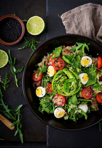 Menu dietetico. Sana insalata di verdure fresche - pomodori, avocado, rucola, uova, spinaci e quinoa su una ciotola. Disteso. Vista dall'alto.