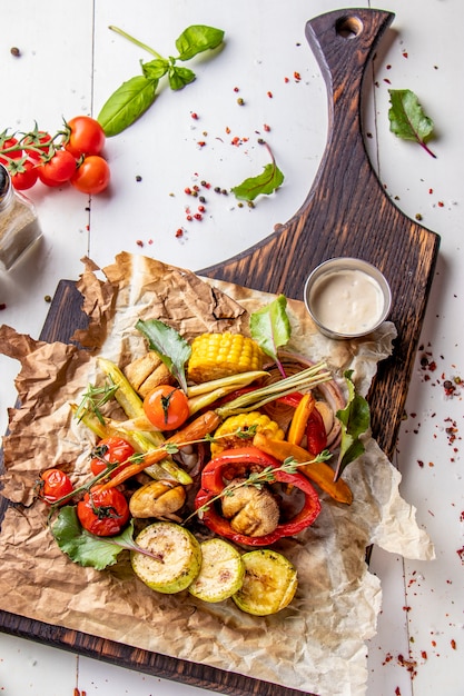 Menu Vegan Grill, verdure grigliate - zucchine, paprika, pomodorini, mais, carote e champignon serviti su tavola di legno