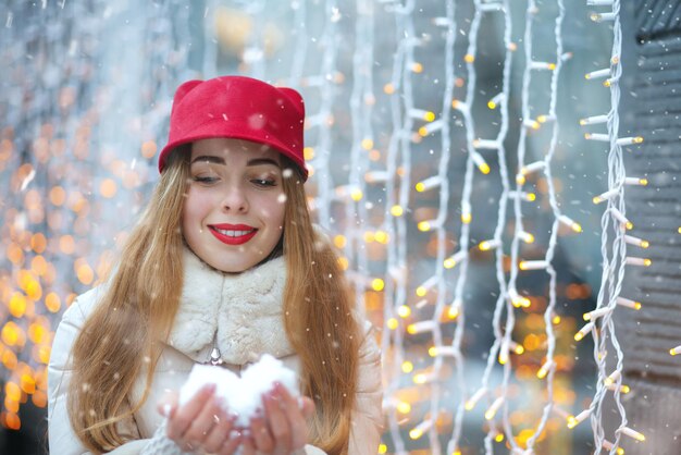 Meravigliosa donna sorridente che tiene la neve tra le mani sullo sfondo di ghirlande. Spazio per il testo