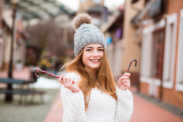 Meravigliosa giovane donna dai capelli rossi in abbigliamento alla moda che tiene in mano un gustoso bastoncino di zucchero natalizio