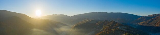 Meraviglioso paesaggio di montagna. Alba nei Carpazi autunnali, i raggi del sole che splendono sulla nebbia e gli alberi gialli autunnali. Vista drone.