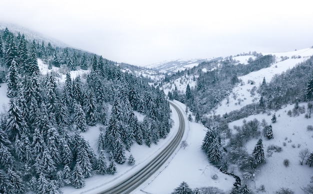 Meraviglioso paesaggio di montagna invernale, strada di montagna innevata con curve e una foresta all'orizzonte.