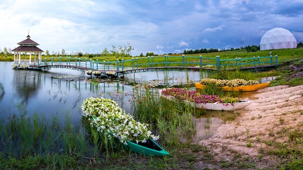 Meraviglioso paesaggio estivo e luogo di meditazione. Un gazebo in legno, una piattaforma e diverse piccole barche piene di fiori in riva al lago.