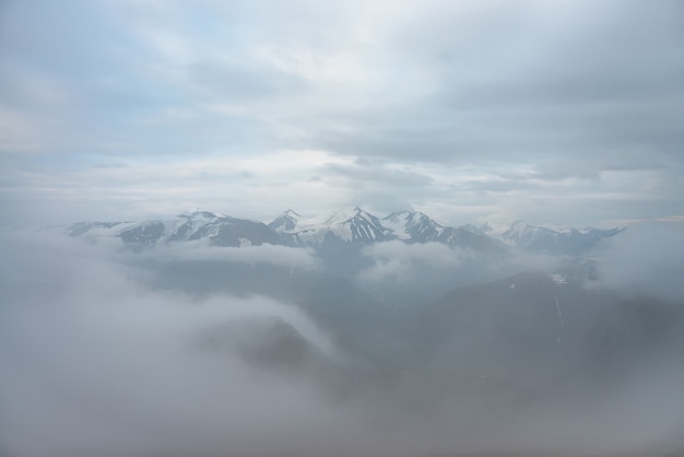 Meraviglioso paesaggio minimalista con tre grandi cime innevate sopra nuvole basse. Minimalismo atmosferico con grandi cime innevate nel cielo nuvoloso. Vista impressionante su montagne innevate fantastiche