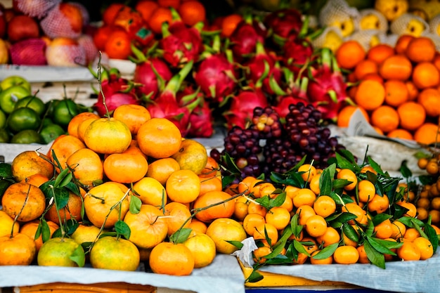 Mercato agricolo asiatico che vende frutta fresca in Vietnam. Mandarino, uva e frutto del drago. Colori arancione e rosso.
