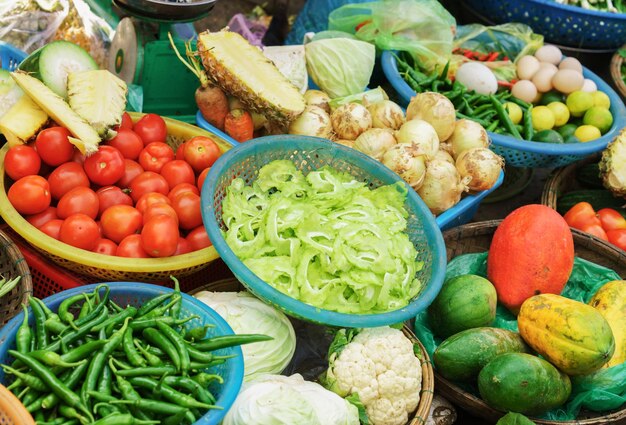 Mercato asiatico degli agricoltori di strada che vende frutta e verdura fresca a Hoi An, Vietnam. Pomodoro, peperone, cavolo cappuccio, cipolla e ananas. Colori verde, rosso e giallo.