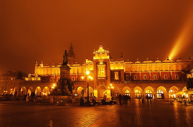 Mercato coperto nella piazza principale di Cracovia di notte nebbiosa con cielo dorato e monumento di Adam Mickiewicz