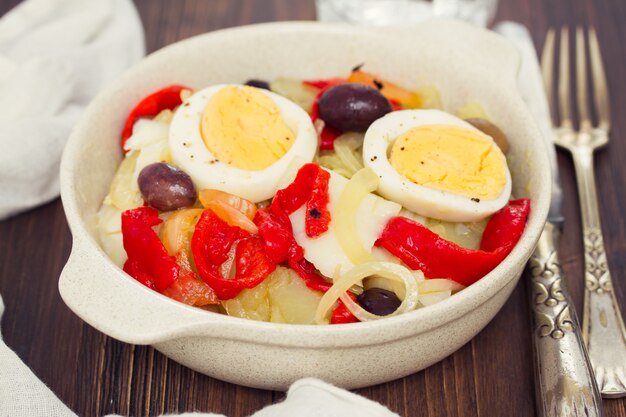 Merluzzo con patate, peperone, uovo e olive sul piatto