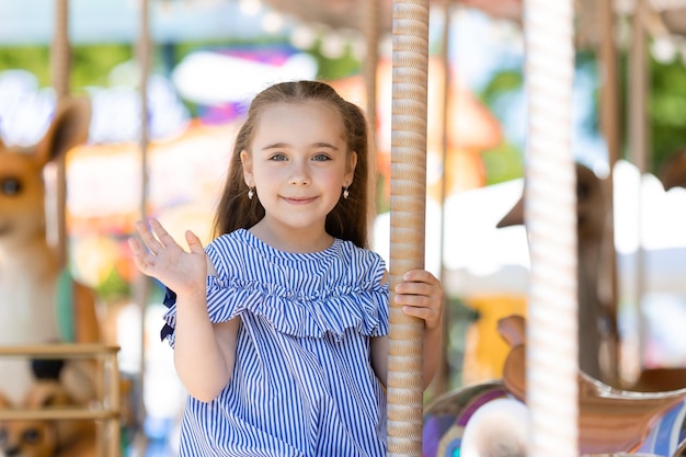 Merrygoround bambina carina in abito blu che gioca sulla giostra al parco divertimenti