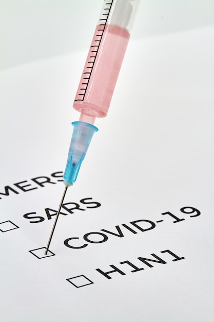 MERS, SARS, COVID-19, H1N1 scritti su un foglio e una siringa