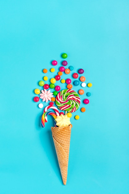 mescolare dolci al cioccolato colorati versati dal cono di cialda gelato su blu piatto laici