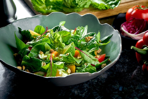 Mescolare l'insalata con cachi, mozzarella, spinaci e noci, serviti in una ciotola verde su un tavolo di marmo scuro. Insalata vegetariana. Cibo del ristorante