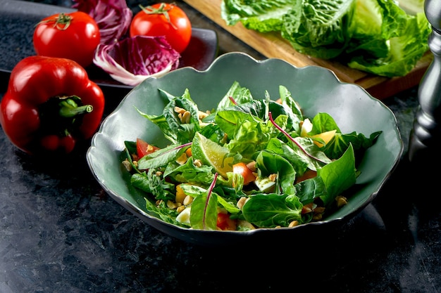 Mescolare l'insalata con cachi, mozzarella, spinaci e noci, serviti in una ciotola verde su un tavolo di marmo scuro. Insalata vegetariana. Cibo del ristorante