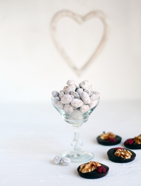 Mescolare le noci in vetro trasparente con anelli di cioccolato su sfondo bianco con cuori - gustosi dolcetti