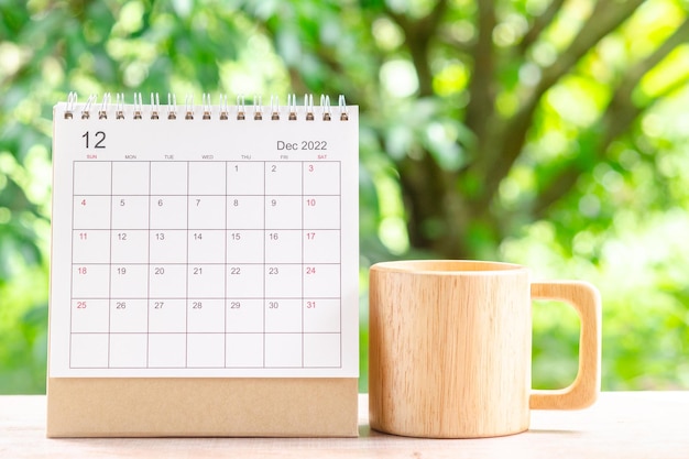 Mese di dicembre, scrivania del calendario 2022 per l'organizzatore alla pianificazione e tazza di caffè in legno sul tavolo di legno con sfondo verde della natura.