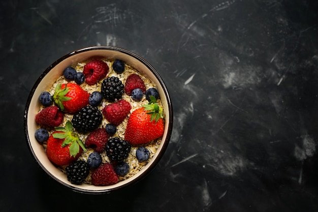 messa a fuoco selettiva, corretta alimentazione, colazione sana, piastra profonda con cereali, farina d'avena, fragole fresche, lamponi, mirtilli e more