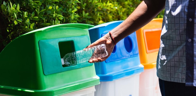 Messa a fuoco selettiva da vicino la mano nera dell'uomo che lancia una bottiglia d'acqua di plastica vuota nel cestino o nel cestino dei rifiuti riciclati, concetto di riciclaggio ambientale