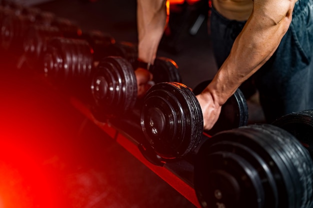 Messa a fuoco selettiva delle mani dei giovani in forma che prendono i manubri dallo scaffale Maschio forte in palestra