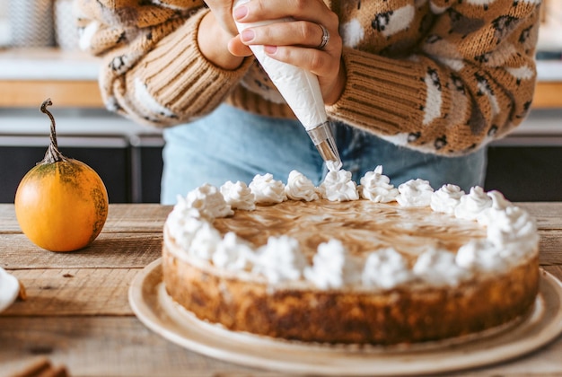 Messa a fuoco selettiva di mani femminili che decorano una gustosa cheesecake di zucca con crema